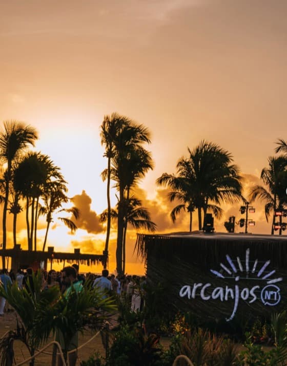 Público em festa ao pôr do sol em um espaço à beira-mar